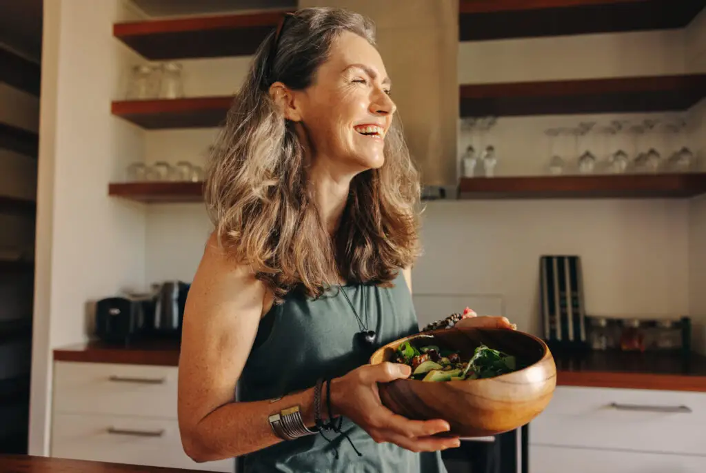 happy woman holding bowl full of leafy greens