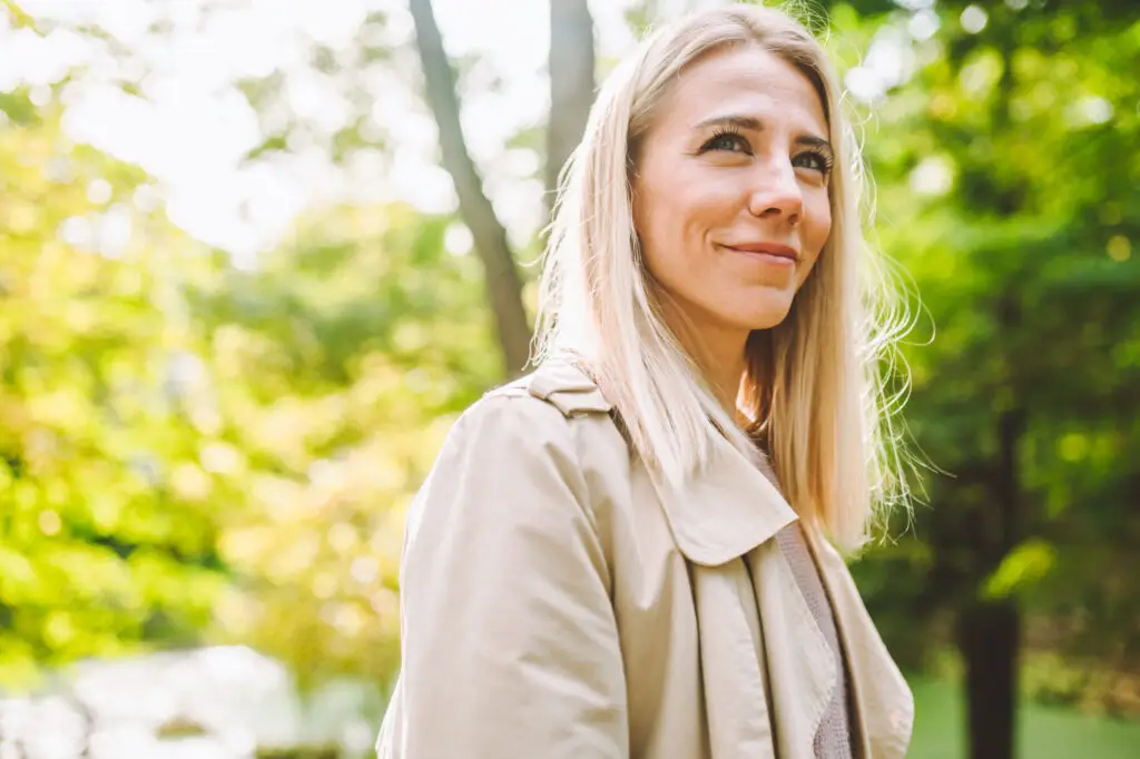 blonde woman smiling happily on sunny summer or spring day outside walking in park