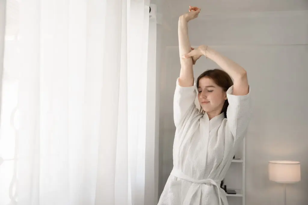 Young woman in white bathrobe doing light morning stretching.