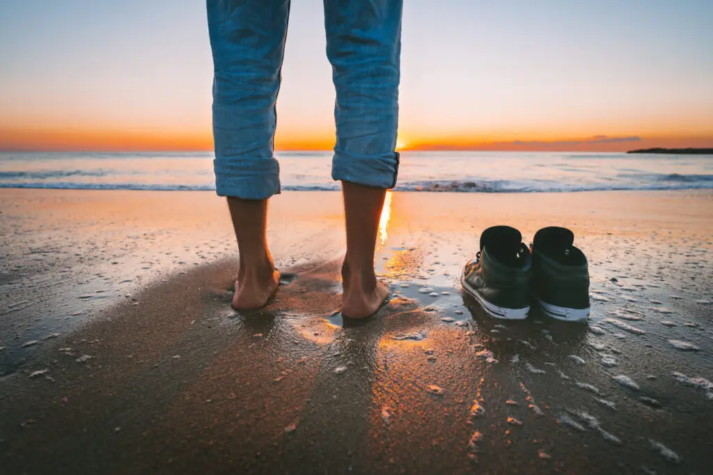 Closeup of barefoot man walking on the summer beach at sunset
